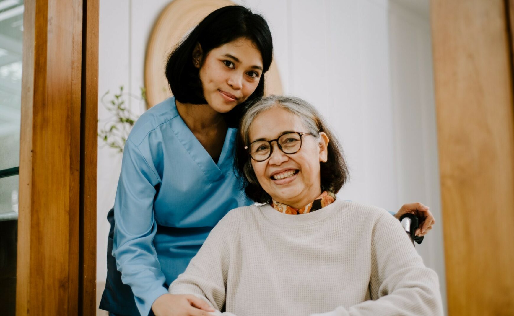 Caregiver standing behind elderly woman who is smiling and sitting in wheelchair