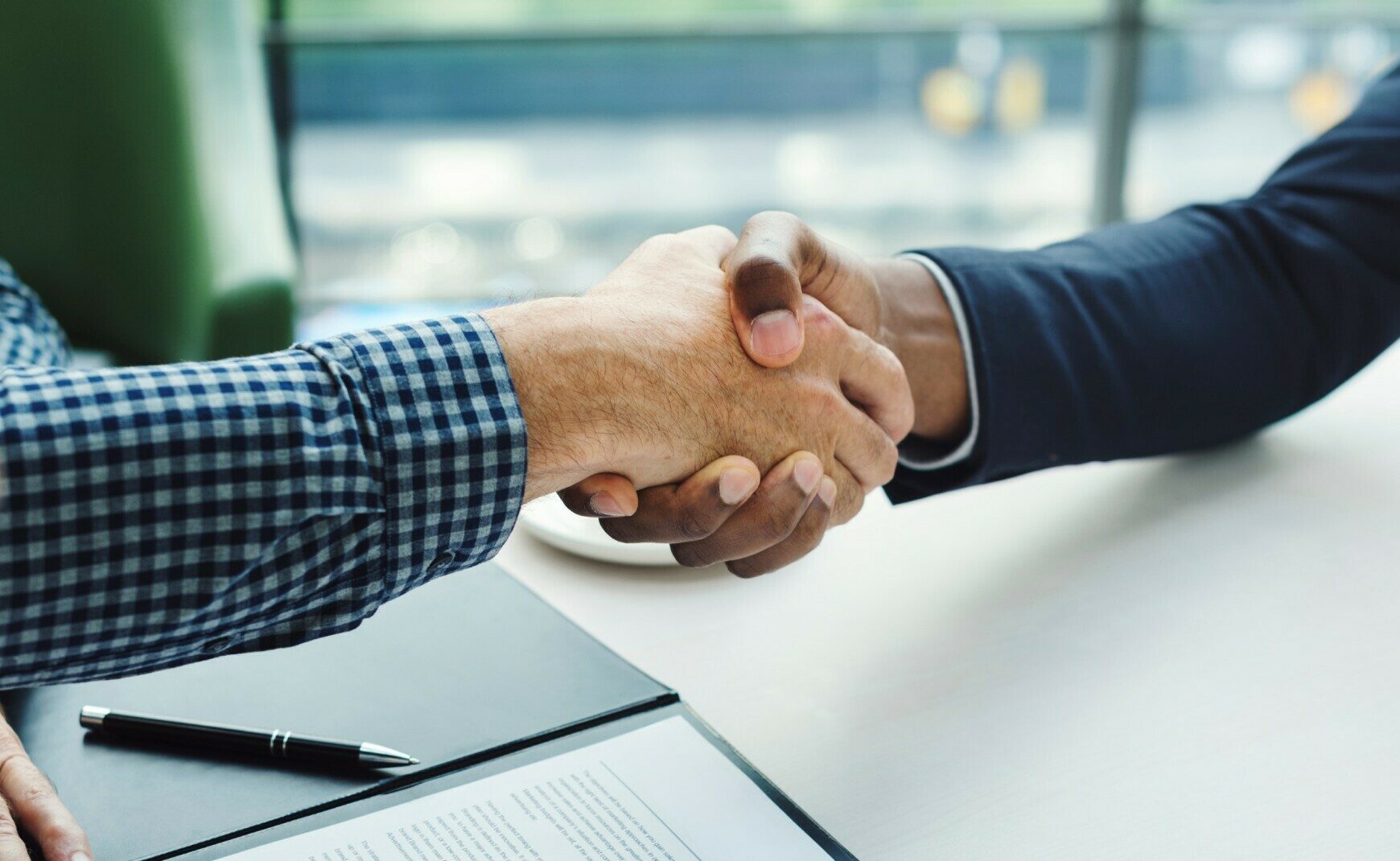 Handshake with pen and paper in background