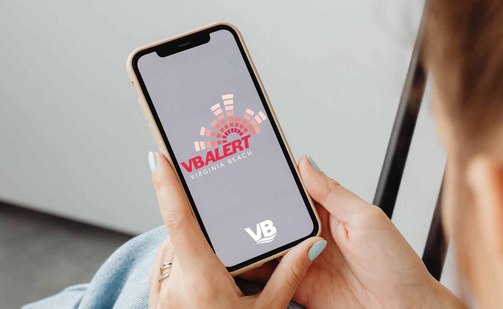 Woman holding cell phone with VB Alert logo and City of Virginia Beach logo