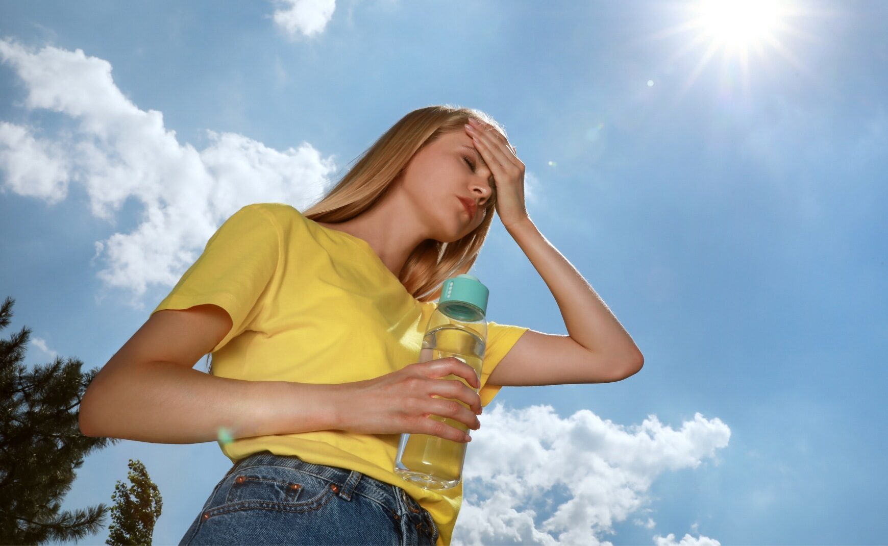 Woman holding water bottle feeling symptoms of heat exhaustion