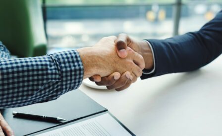 Handshake with pen and paper in background