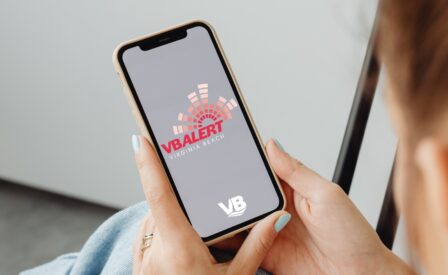Woman holding cell phone with VB Alert logo and City of Virginia Beach logo