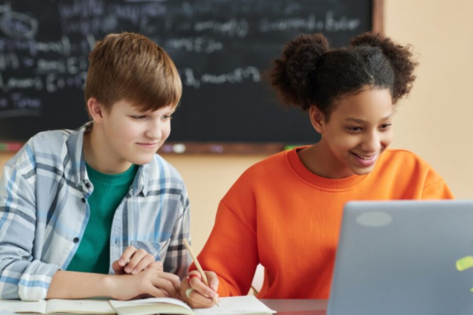 School aged boy and girl working on assignment with laptop and notebook