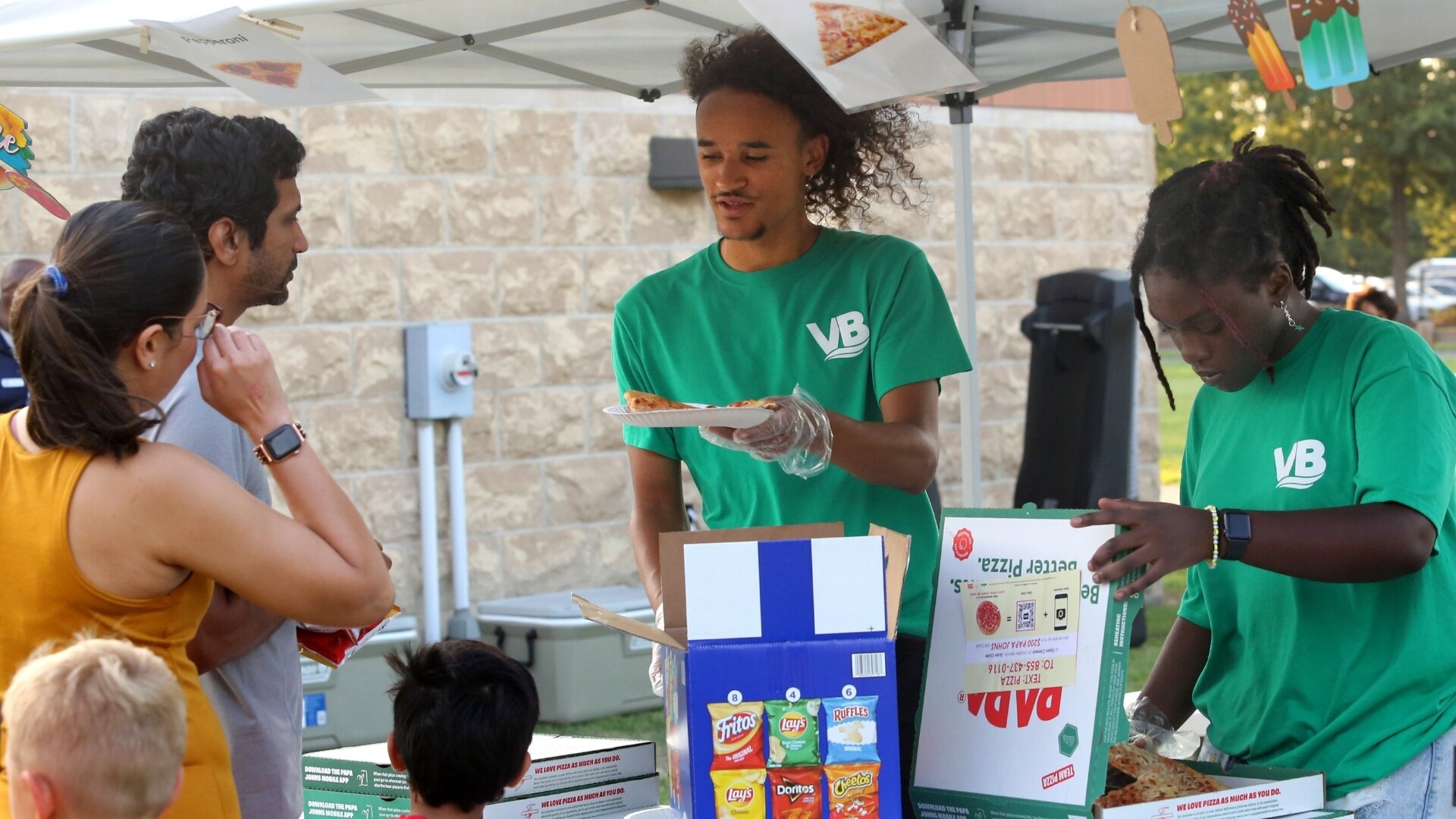Parks and Rec employees serving pizza to family in line