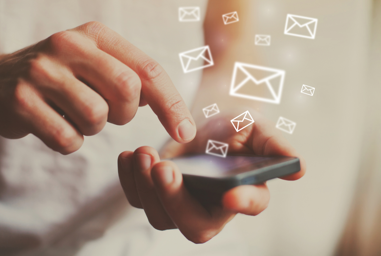 Person holding phone with email envelopes flying off screen