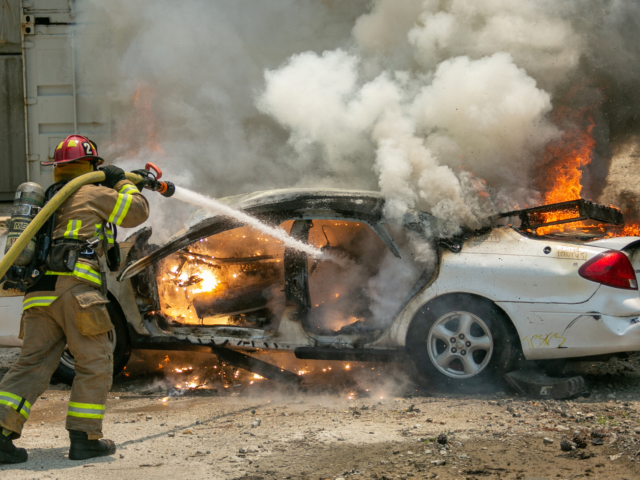 Firefighter hosing down white car on fire during training exercise