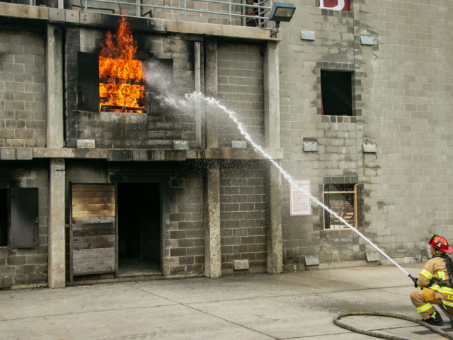 Window on fire at burn practice building with firefighter putting it out