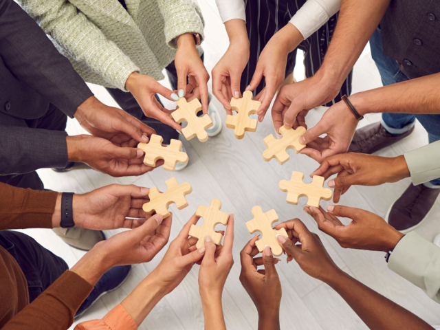 Group of individuls in circle holding puzzle pieces together