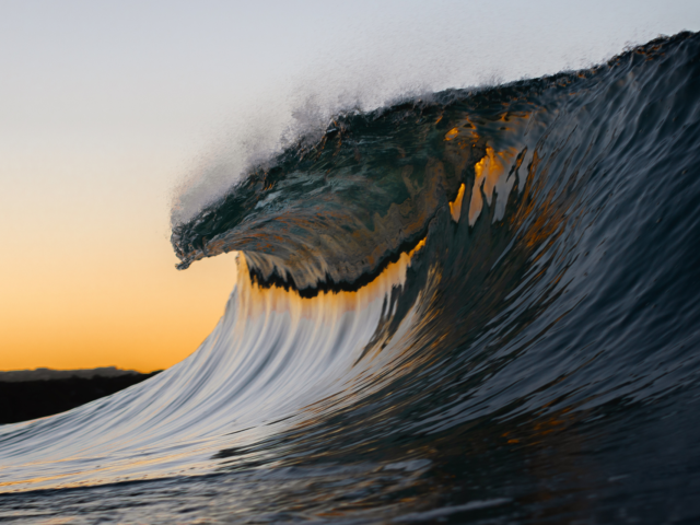 Ocean wave cresting with sunrise in background