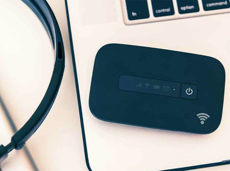 A black Wi Fi hotspot on a laptop keyboard with a headset nearby