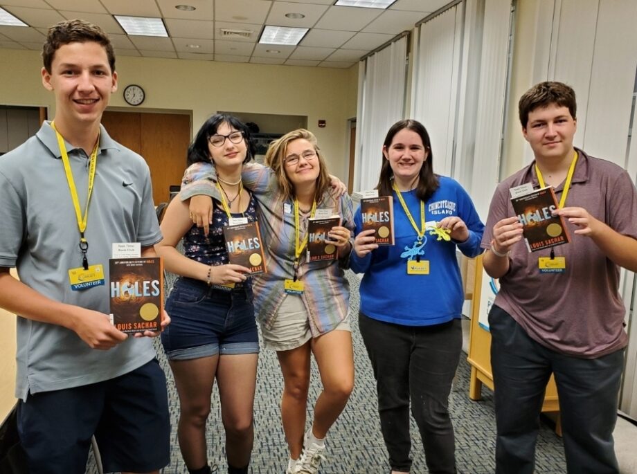 Five teen library volunteers posing and holding copies of Holes