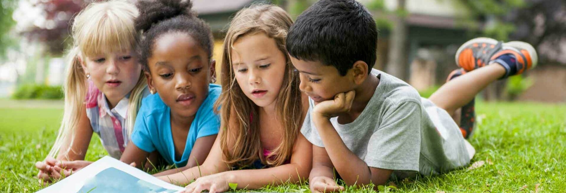 Summer kids reading a book while lying on grass