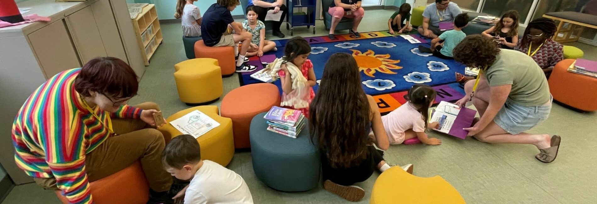 Group of children and adults in Library activity room with books
