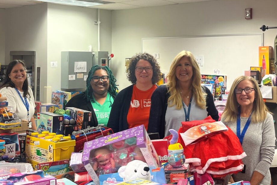 Five women of diverse backgrounds and ages stand in front of a large stack of toys