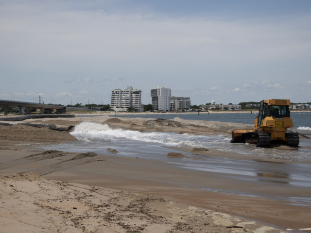 Earth mover hauling sand near waterline on beach