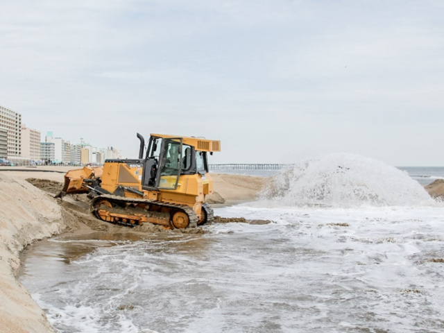 Earth mover plowing sand along beach