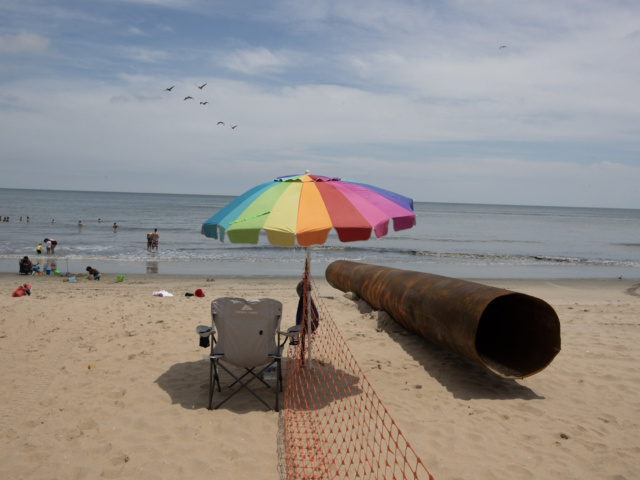 Rainbow beach umbrella and chair next to dredge pipe and safety fence on beach